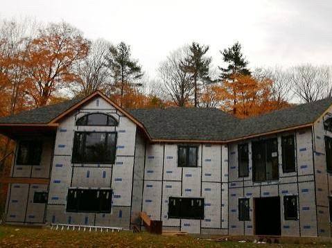 New-build home wrapped and framed, roof shingled, autumn trees behind